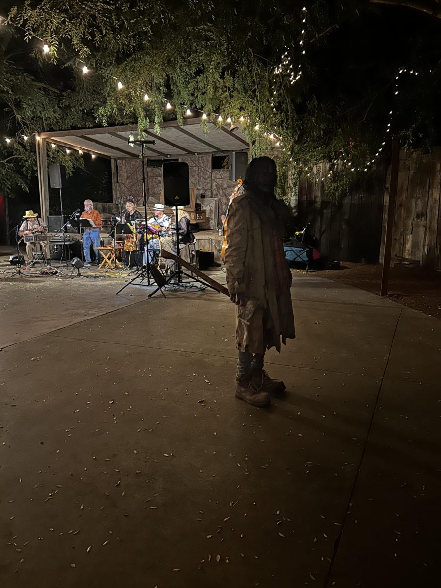 An individual dressed up as a zombie lurks  in the center of Hobbs Grove as a band plays haunting music in the back.