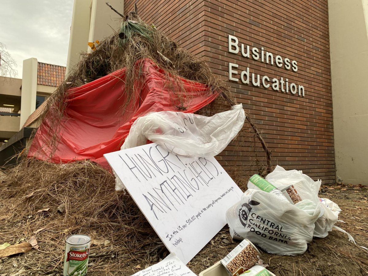 The unhoused encampment art piece sits outside the Business Education building with bags of food in front on Nov. 22. Photo by Logan Payne.