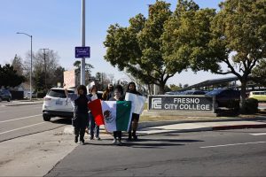 Protesters walk towards Blackstone from McKinley Avenue silently holding their signs and flag passing a Fresno City College sign on Feb. 11, 2025